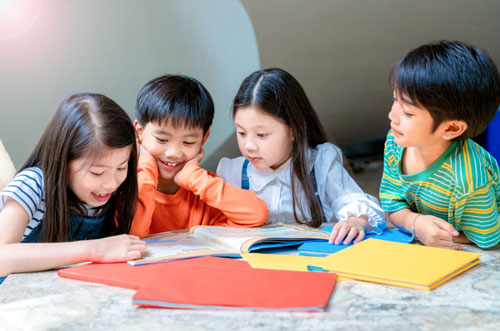Four Asian children sitting at a table looking at a book