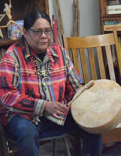 Native American man sitting in a chair at the Sierra Native Alliance and playing a drum