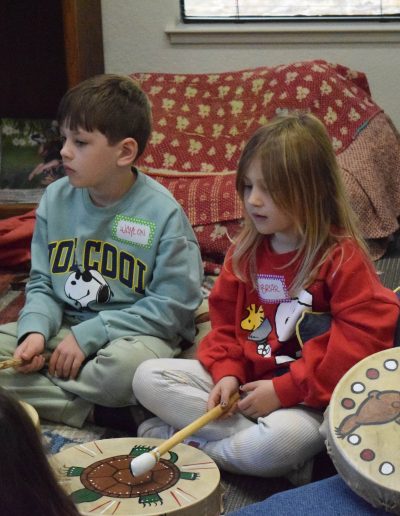 Two kids sitting on the floor at the Sierra Native Alliance with Native American drums in front of them