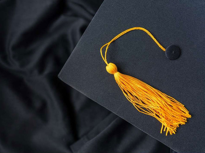 capgown closeup photo showing part of a mortarboard with yellow tassle on top of a graduation gown