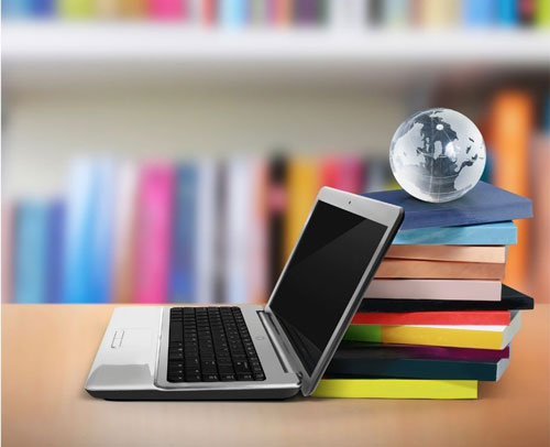photo of a laptop computer open with the screen leaning against a stack of books with a globe on top