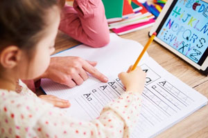 closeup photo of a young girl at a desk learning to write the letter A